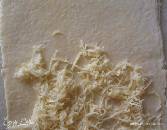 Раскатываем 1/4 часть теста прямоугольником.
( удобнее работать с тестом по частям ).
Раскатываем не очень тонко. На одну часть кладем тертый сыр полторы-две  ст ложки.