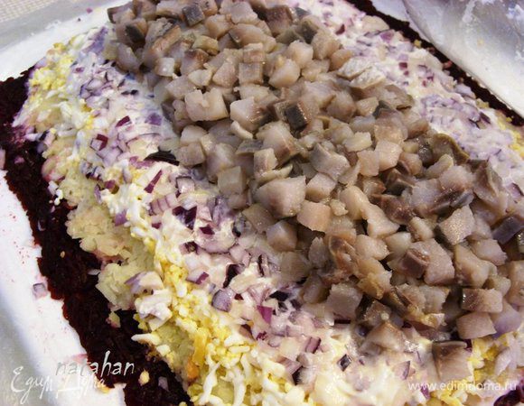 По середине лукового слоя выложить полосой мелко нарезанные кусочки сельди. Немного утрамбовать их ладошкой через целлофан.