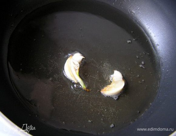 Картофель вымыть со щеткой, нарезать кружочками, толщиной около 3-5 мм. Разогреть половину растительного масла, очистить чеснок, разрезать вдоль на 2 половинки и обжарить 1-2 минуты до румяности. Выложить в миску.