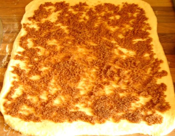 Поднявшееся тесто раскатать в прямоугольник на присыпанной мукой поверхности. Равномерно распределить начинку, оставив на узкой стороне не промазанную полоску теста (3-5 см).