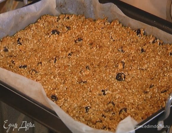 Выстелить противень с высокими бортами бумагой для выпечки, смазать ее оставшимся сливочным маслом, выложить овсяную смесь, плотно утрамбовать и отправить в разогретую духовку на 30 минут.