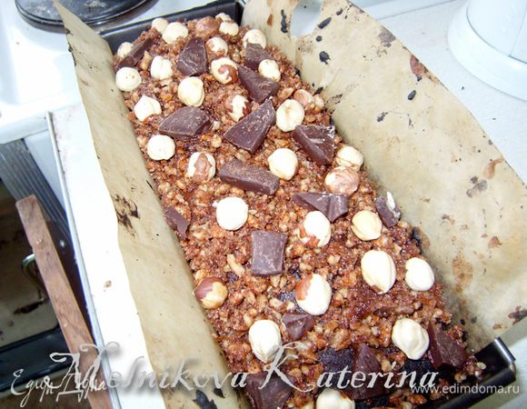Тем временем подсушить немного фундук в микроволновой печи (1 минута), очистить от шелухи. Вынуть кекс из духовки. Выложить оставшуюся ореховую смесь, разровнять. Сверху выложить цельный фундук и поломать кусочки шоколада. Отправить в духовку еще на 10 минут. 