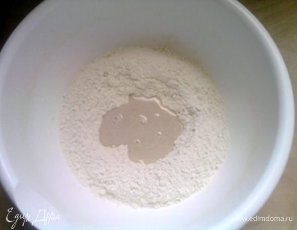 Муку насыпать горкой (удобнее в миске). Сделать углубоение в центре и влить 60 мл тёплой воды. Добавить в воду дрожжи. Смешать их с водой (муку не подмешивать), накрыть крышкой и оставить на 10 минут.