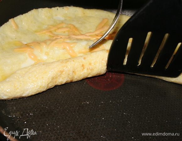 Выкладываем семгу с одного края. Поддеваем этот край омлета лопаточкой. Начинаем аккуратно сворачивать омлет в рулет, завернув туда семгу.