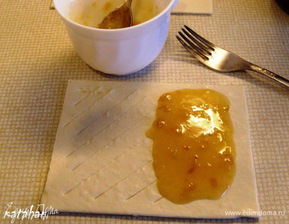 Каждый пласт слоёного теста поперёк разделить пополам - получится 12 пластиков размером 10х10см. В кружку с абрикосовым джемом положить крахмал, тщательно перемешать. У 6 пластиков левую половину через 1 см разрезать острым ножом наискосок, не доходя до края по 1 см. На правую половину выложить по 2 ч.л. абрикосового джема, разровнять по половинке пластика не доходя до края на 1 см.