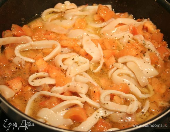Добавьте кольца кальмара и томаты на сковороду, добавьте немного соли, базилика, чесночную кашицу и готовьте 5 минут.