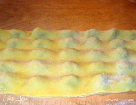 Накрыть второй половиной теста. Теперь очень важно дать выйти воздуху, чтобы готовые равиоли не лопнули при варке. Для этого, нажимая пальцем, сдавить тесто между будущими равиоли,намечая их форму, начиная от центра и двигаясь к краям. 