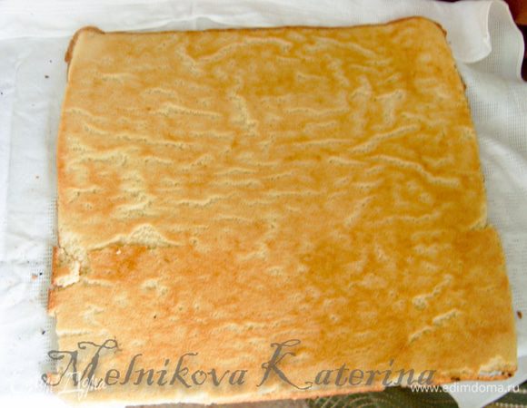 Застелить стол кухонным полотенцем, посыпать 1 ст.л. сахара и выложить теплый бисквит пергаментом вверх. 