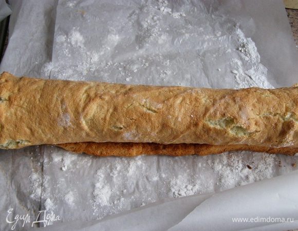 Как только бисквит испечется, выложим его на пергаментный лист, присыпанный сахарной пудрой. Аккуратно снимем пергамент, на котором бисквит пекся. Пергамент снимается очень легко, нужно только слегка потянуть за край. Минут через пять свернем бисквит в рулет.