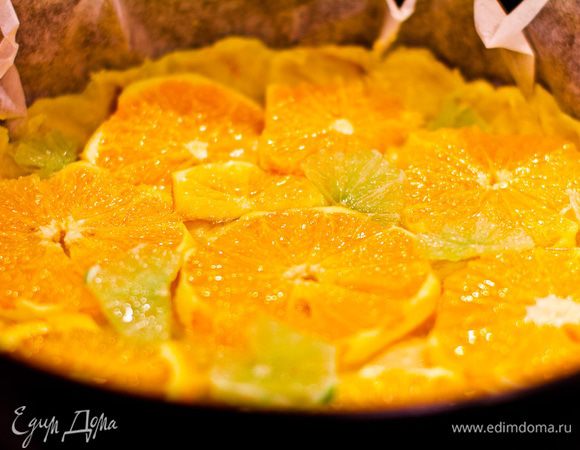 Всыпьте муку и апельсиновую цедру, замесите тесто. Разделите тесто на две неравные части. Застелите форму пергаментом. В форму выложите большую часть теста, разровняйте, сделайте бортик. На ней разместите кружочки апельсина и лайма.