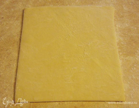 Посыпьте стол мукой и положите один размороженный пласт теста.