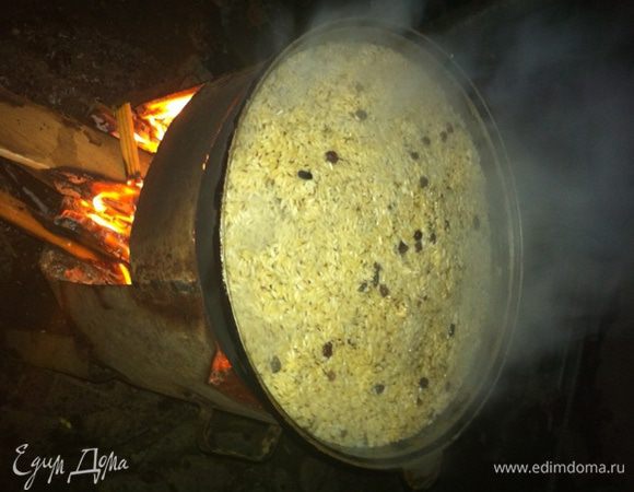 Добавьте дров в очаг и начинайте выпаривать жидкость, одновременно перемешивая слой риса.