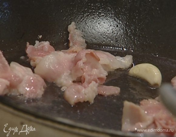 В глубокой и тяжелой сковороде разогреть оливковое масло и обжарить бекон до золотистого цвета, добавив к нему чеснок целиком.