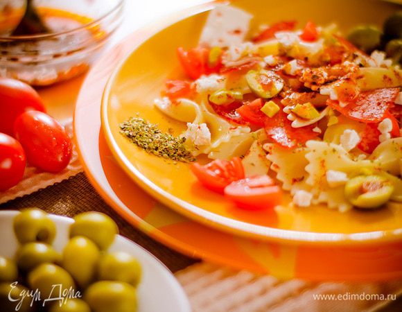 Фету разломите руками, оливки разрежьте пополам. Смешайте бантики с кусочками салями, дольками помидоров и оливками. Приготовьте соус: смешайте оливковое масло, молотую паприку, орегано, соль и перец. Залейте салат соусом и слегка перемешайте. Сверху посыпьте фетой.