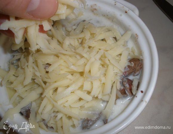 Разложить печенку с луком по керамическим формочкам, залить все соусом и посыпать сыром. Запекать в духовке до золотистой корочки около 20 минут. Подавать с зеленью.