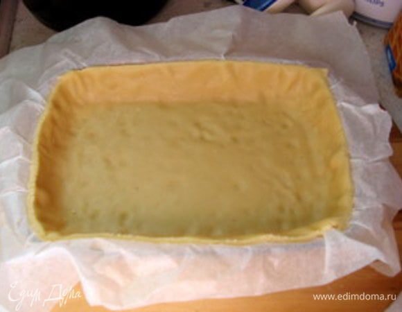 Раскатать тесто на пергаменте в прямоугольник. Перенести его в форму для выпечки вместе с пергаментом. Обрезать излишек теста, выходящий за пределы формы.