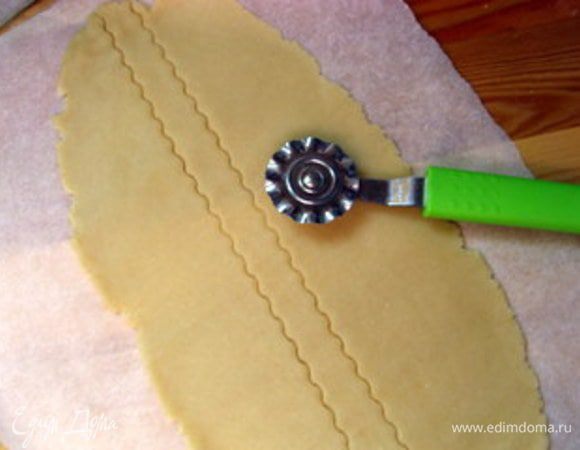 Снова раскатать срезанное тесто. Это удобно делать между двух листов пергамента. Колёсиком с зигзагом нарезать тесто на полоски. Взбить яйцо.