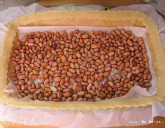 Накрыть тесто пергаментом. Высыпать сверху фасоль и выпекать при 180° около 15-20 минут.Достать готовую основу и слегка остудить.