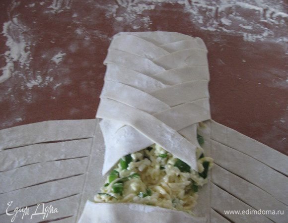 Затем переплетаем на начинке тесто, укладывая друг на друга попеременно то левую, то правую полоски. Между полосками должно оставаться небольшое пространство, для того, чтобы пар, испускаемый во время выпекания, мог свободно выходить наружу. Не доходя пару полосок до края   загибаем вторую часть средней полосы и  заканчиваем полосками. 