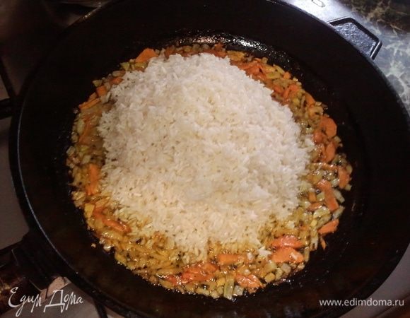 На разогретую тяжелую толстостенную сковороду налить растительное масло( я обычно часть специй и одну раздавленную дольку чеснока добавляю в это горячее масло еще до всего- чеснок вынимаю перед закладкой овощей), затем обжарить морковь и лук до золотистого цвета. В середину сковороды выложить рис и разровнять его таким образом, чтобы лук и морковь распределились по бортикам сковороды( это легко получается!)Следует учитывать, что блюдо увеличивается в объеме примерно на треть!