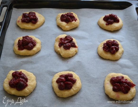 Отрываем кусочек теста, катаем колобочек, и выкладываем на противень прижимая пальцами в лепешку, сверху кладем вишню.