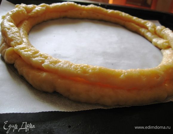 Рисуем на пергаменте круг диаметром 20-23 см по желанию. Кондитерским мешком выкладываем круги из теста. В идеале их должно быть 3, 2 основных и 1 сверху, как на фото. Рядом из оставшегося теста выкладываем профитроли.  Ставим в духовку и выпекаем при 180 градусах 40-50 минут. Духовку не открывать!