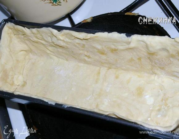 Слоеное тесто разделить на две части, одну немного больше другой. Взять бОльшую часть, раскатать на присыпанной мукой поверхности в прямоугольник и выстелить прямоугольную форму для выпечки так, чтобы тесто заполнило дно и бока формы.