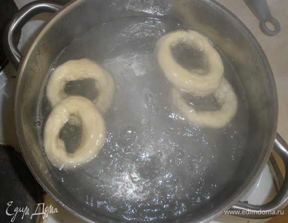 В кастрюле вскипятить воду, опускать туда бублики на 15-20 секунд. Они сразу всплывут. Вытащить их шумовкой и уложить на противень (на нем заранее растелить пергамент и смазать его маслом - я использовала свой любимый многоразовый коврик).