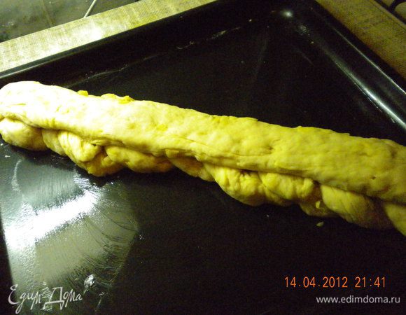 Разделить тесто на 4 части: три одного размера и одну немного больше. Из трех равных частей скатать длинные тонкие жгуты, примерно 70 см в длину (у меня получились покороче,см40, как раз косичка поместилась на противень). Выложить их на пергамент и сплести в нетугую косу. Оставшееся тесто скатать в жгут такой же длины как получившаяся косичка,положить его сверху и слегка прижать к косичке.