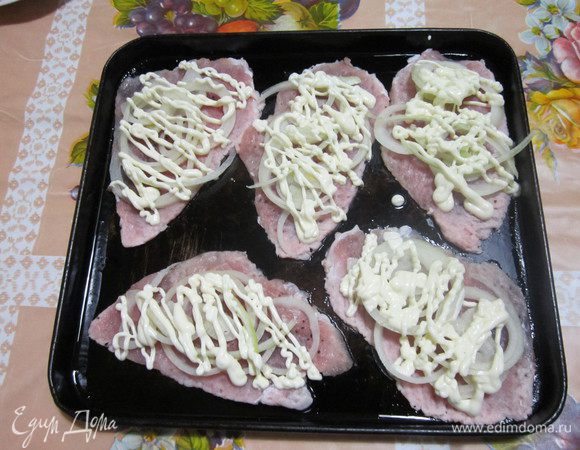 Отбитые кусочки мяса выкладываем на смазанный маслом противень. Сверху- колечки лука и смазываем майонезом.