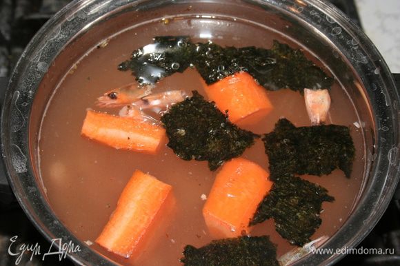 Почистить морковку. Панцири от креветок положить в кастрюльку с водой, туда же добавить морковь и поломанный на кусочки лист нори. Варить бульон 20 минут.