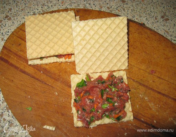 Вафельный корж разрезать на квадраты или треугольники. На одну часть положить фарш, накрыть второй.