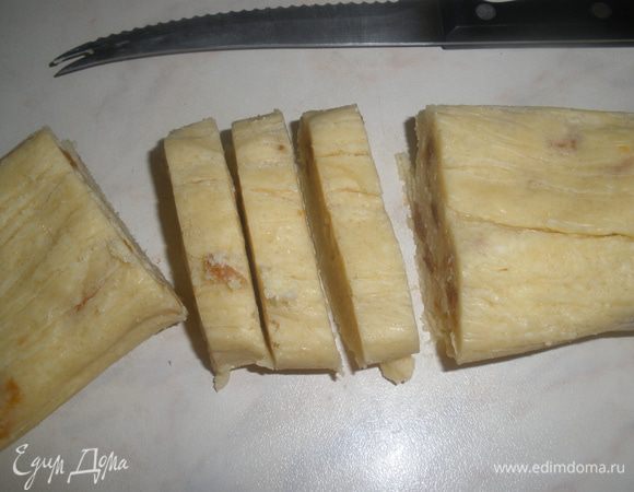 Убрать пленку, нарезать колбаску на ломтики толщиной 6 мм. Уложить на застеленный бумагой для выпечки противень. 