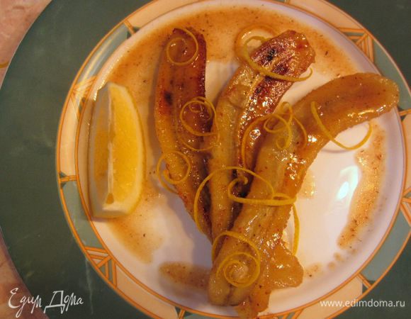 Через пару минут выложите бананы в тарелку. Долейте в сковороду вторую порцию спиртного и уварите соус пополам. Процедите соус через сито. Полейте сверху на бананы. Снимите немного цедры с лимона (я это делал специальным ножом). Выложите к бананом дольку лимона.