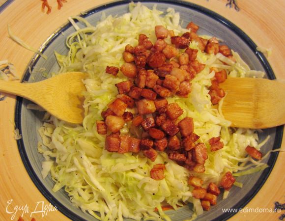 Пока капуста горячая, снимите сковороду с грудинкой с огня, выложите грудинку вместе с вытопившимся жиром в капусту и перемешайте. Проще всего это делать двумя лопатками.