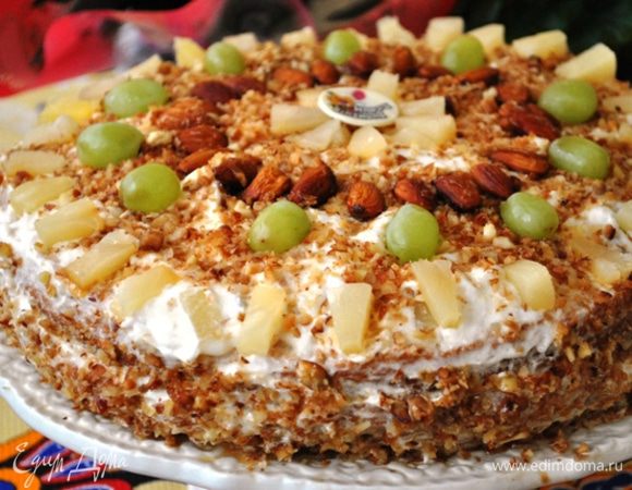 Верх и бока обильно смазываем кремом, украшаем ананасами и посыпаем грильяжем.