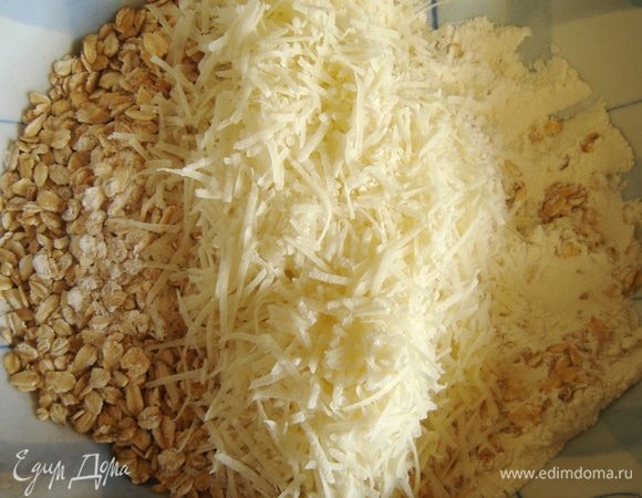 Смешать муку, овсяные хлопья, тёртый пармезан и соль. Если используются обычные овсяные хлопья, то готовое тесто будет хрустящим. Тонкие хлопья пропекаются полностью. Масло нарезать на кубики и растереть с мучной смесью. Добавить орешки и семечки.