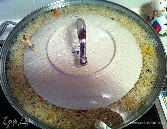Когда жидкость полностью впитается в рис, делаем лунки в рисе для чеснока и пристраиваем его там. Последний раз разравниваем рис, немного убирая рис с краев в сторону центра и собирая в пологую горку. Делаем 3-5 отверстий до дна казана. Накрываем, заранее приготовленной, тарелкой рис и закрываем Вок крышкой (без отверстий). Делаем температуру на  1 (минимум) и ждем примерно 25 минут. (Для того что бы понять примерно какое время держать плов закрытым, попробуйте рис с шумовки (он наверняка там остался), если рис почти готов лучше уменьшить время ожидания до 18-15 минут, если еще сыроват, то лучше подождать 25 минут)