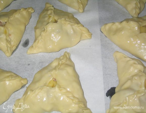 Выложить треугольники на противень, застеленный бумагой для выпечки. Ели нет бумаги, то можно и без нее, т.к. тесто достаточно маслянистое. В центр каждого треугольника вложить кусочек сливочного масла, а также смазать их поверхность растопленным маслом.