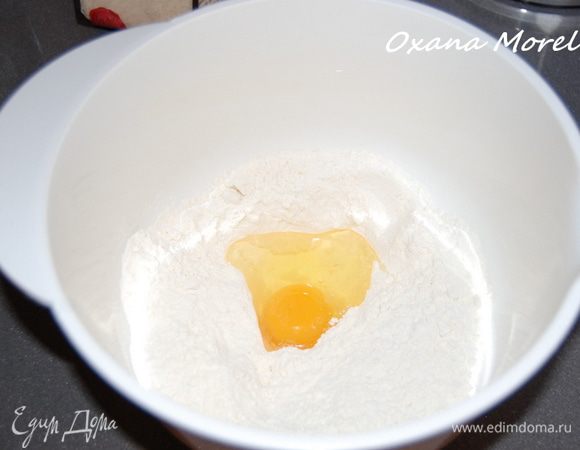 Муку просеять горкой, в центре сделать углубление и вбить яйцо, добавить оливковое масло, сахарную пудру и ванилин.