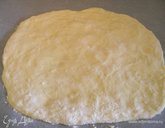 Достаем наше тесто и раскатываем его. Удобно это делать сразу на бумаге для выпечки. Я свое не раскатывала, просто пальцами разровняла его по поверхности.
