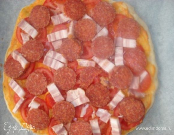 Затем слоем выложить кружочки помидоров, порезанный брусочками бекон и порезанную кружочками колбасу