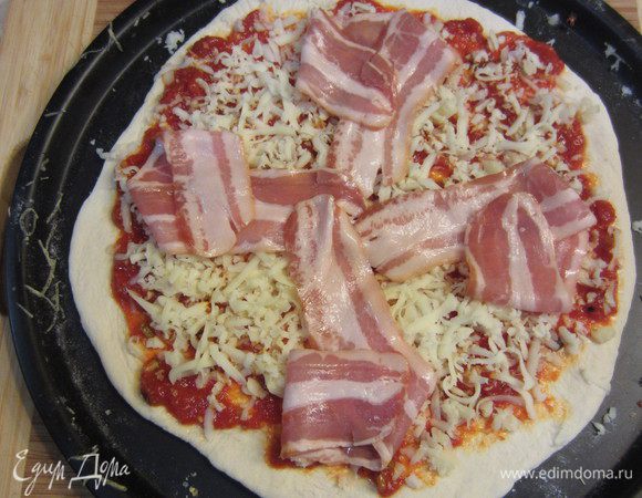 Готовим тесто и соус по предыдущему рецепту. Нагреваем духовку до максимальной температуры. Выкладываем соус поверх раскатанного теста. На соус выкладываем порцию моцареллы. Поверх моцареллы кладем ломтики бекона. Замечательно будет, если вы сложите из них что-нибудь эдакое, чтобы часть бекона была в воздухе. Она хорошо зажарится, что обогатит вкус пиццы. Ставим пиццу в духовку и ждем, пока приготовится.