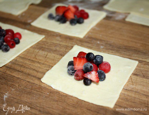 Пласт теста раскатать на присыпанной мукой поверхности.Разрезать на квадраты со стороной 7 см(всего около 32 квадрата).Свежую клубнику нарезать на небольшие кусочки,остальные ягоды(у меня мороженные)добавить целыми.На 16 квадратов выложить по 1 десертной ложке ягод.