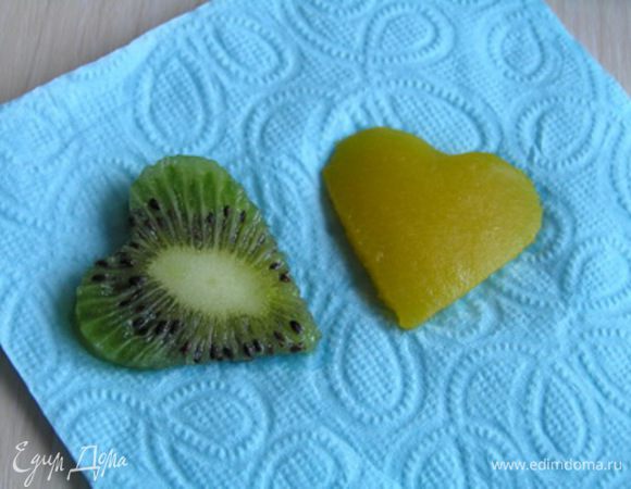 Аккуратно достать пирожные из колец, снять бумагу. Из кусочков киви и манго вырезать сердечки, обсушить на салфетке.