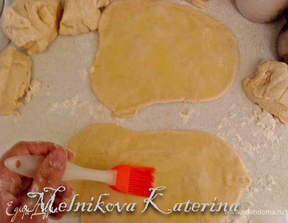 Затем раскатать две части скалкой до толщины примерно 3-5 мм, должны получиться небольшие овалы - прямоугольники. Не бойтесь, что они будут не совсем ровными, от этого погача будет еще "кучерявистей" :) Итак, раскатав две части, их обе нужно смазать сливочным маслом. 