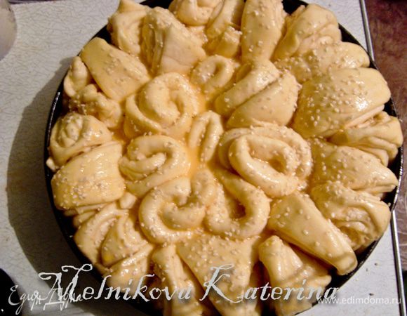 Накрыть погачу тканью и поставить в теплое и укромное место для подхода (примерно 40 минут). В отдельной тарелке смешать желток с молоком. Смазать поверхность хлеба, присыпать кунжутом. 