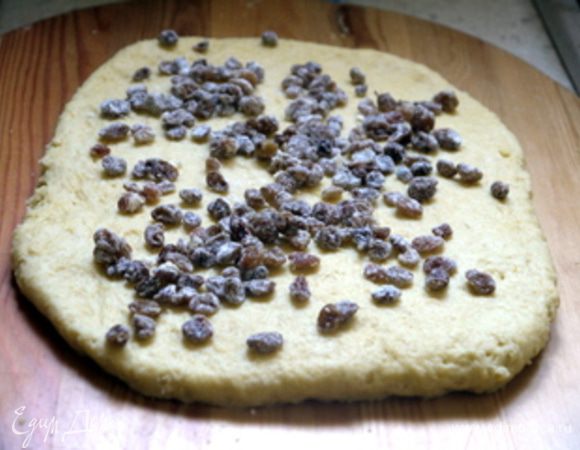 Тесто с помощью скалки слегка раскатать в пласт. Рассыпать изюм по пласту теста, придавить его слегка рукой и выместить тесто с изюмом.