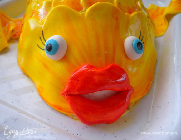 Приклеить (под губки подложить немного белой мастики - зубки) ...Глазки (из белой и голубой мастики), реснички (пищевым фломастером) :-))). В остатки желтой краски капнуть красной и пройтись по основанию чешуек, плавников, хвоста  и по "мордочке"