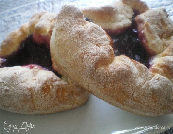 Замесить тесто. Сметану смешать с сахарной пудрой. Затем добавить муку, смешанную с разрыхлителем.  Смесь ягод смешать с сахаром и поставить на огонь. Добавить крахмал. Перемешать. Дать остыть.Раскатать тесто и разложить по формам. Выложить начинку, завернуть края. Поставить в разогретую духовку до 180 С на 30 минут.